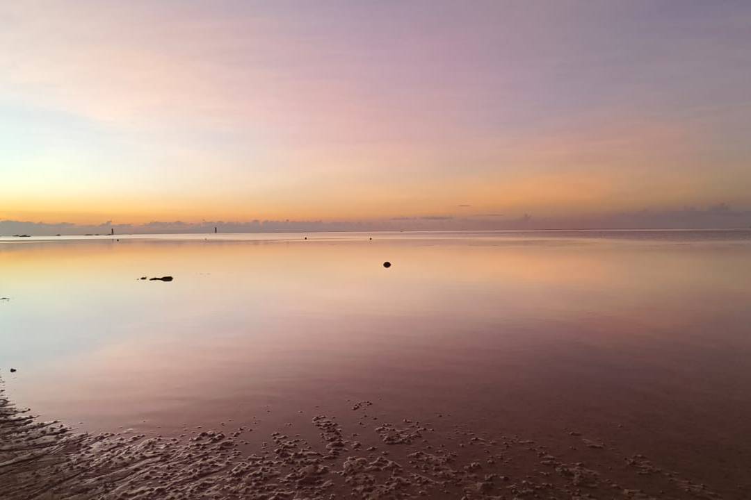 Dawn light spreading across still water at first light, open sky above and a low far shore